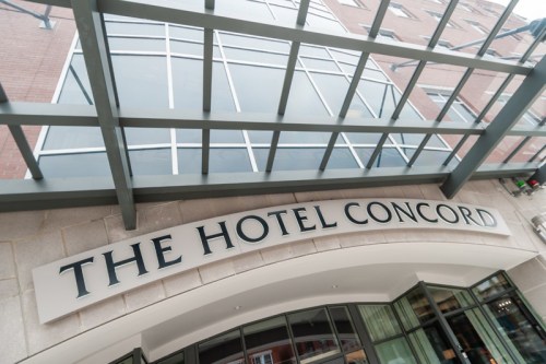 Signage of The Hotel Concord under a modern glass canopy, showcasing the building's entrance.