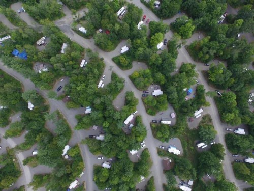 Aerial view of a wooded campground with winding roads and numerous RVs and tents nestled among the trees.