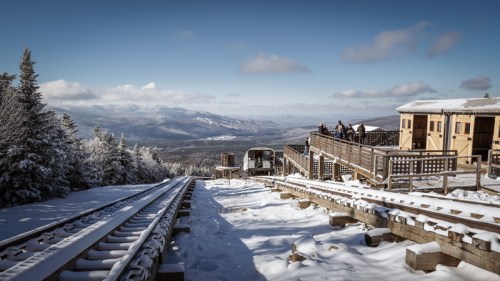 Snow-covered landscape with a mountain view, featuring a railway track and a wooden observation deck.