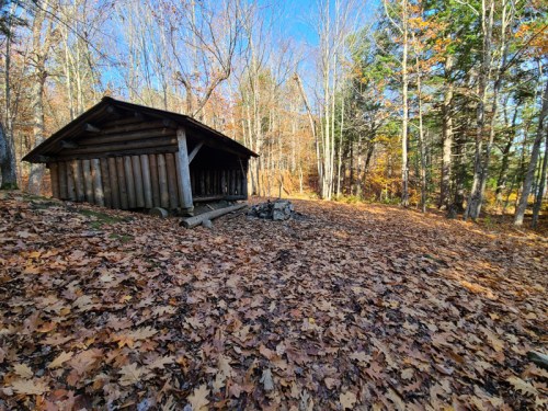 A rustic wooden cabin surrounded by colorful autumn leaves and trees in a serene forest setting.