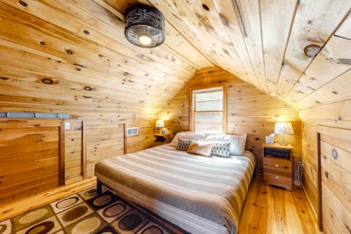Cozy wooden bedroom with a sloped ceiling, a large bed, and warm lighting from lamps on bedside tables.