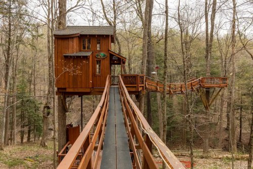 A wooden treehouse connected by a walkway, surrounded by bare trees in a serene forest setting.