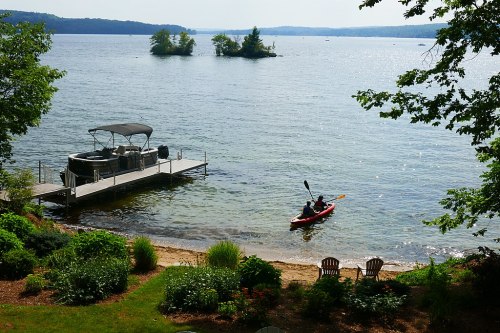 A serene lake scene with a kayak on the water, a dock, and lush greenery along the shore.