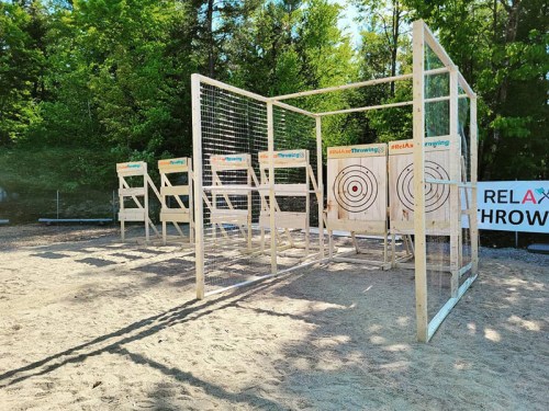 A sandy outdoor area with wooden target boards for throwing activities, surrounded by trees and a sign that says "RELAX Throwing."