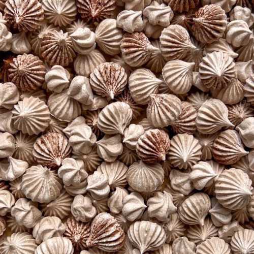 A close-up of various small, intricately shaped meringue cookies in shades of beige and brown.