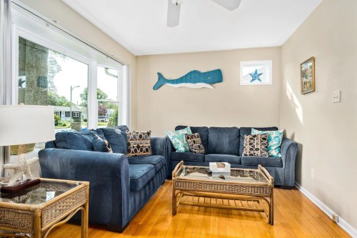 Cozy living room with blue sofas, decorative pillows, a glass coffee table, and a whale wall art. Bright natural light.