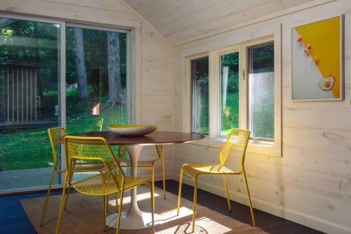 Bright dining area with a round table and yellow chairs, surrounded by large windows and natural light.