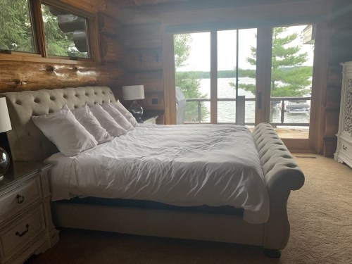 Cozy bedroom with a large bed, wooden walls, and a view of a lake through sliding glass doors.
