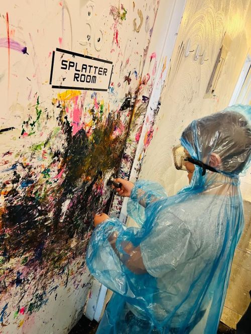 A child in a blue poncho paints a colorful, messy wall labeled "SPLATTER ROOM."