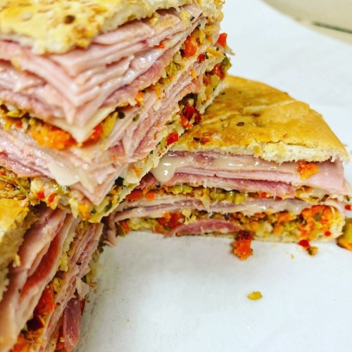 A stacked sandwich with layers of ham, cheese, and a spread, resting on a white surface.