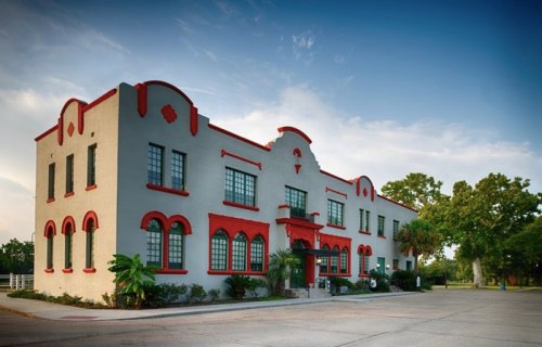 Historic building with red accents, large windows, and palm trees, set against a blue sky.