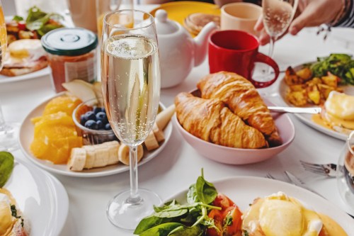 A table set with a variety of breakfast foods, including croissants, fruit, and champagne in a glass.