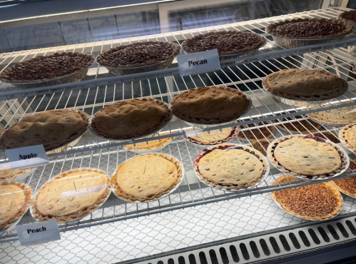 A display case filled with various pies, including apple, peach, pecan, and others, arranged on wire shelves.