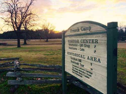 Signpost for French Camp with directions to visitor center, historical area, and amenities, set against a sunset backdrop.