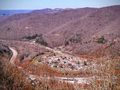 Aerial view of a small town nestled in a valley surrounded by bare, rolling hills in early spring.