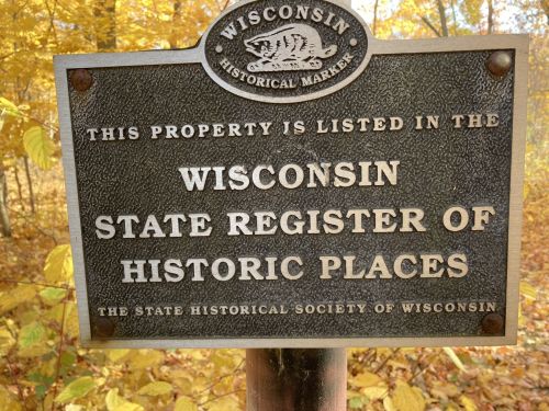 A weathered sign indicating a property listed in the Wisconsin State Register of Historic Places, surrounded by autumn foliage.