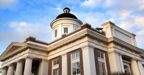 Historic building with a dome, featuring classical columns and intricate architectural details against a blue sky.