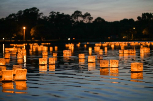 Floating lanterns illuminate a calm lake at dusk, creating a serene and magical atmosphere.