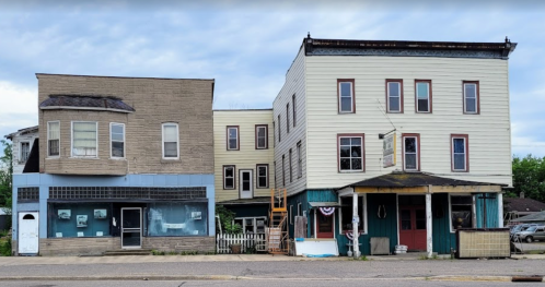 Two old buildings side by side, one with a blue facade and the other in yellow, featuring various windows and a porch.