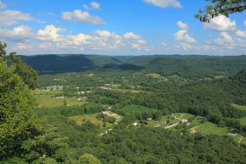 A panoramic view of lush green hills and valleys under a blue sky with fluffy clouds.
