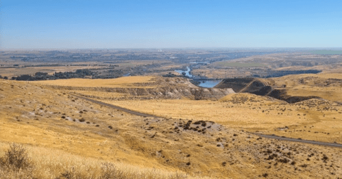 A panoramic view of a dry, golden landscape with a winding river and distant hills under a clear blue sky.