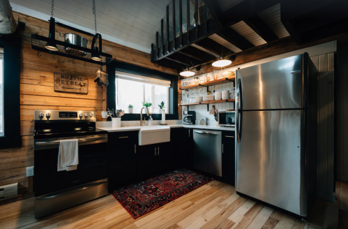 Cozy kitchen with wooden accents, stainless steel appliances, and a farmhouse sink, featuring shelves and a decorative rug.