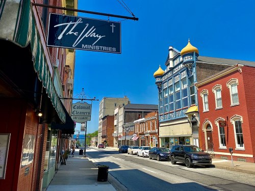 A sunny street scene featuring shops, a church sign, and colorful buildings in a small town.