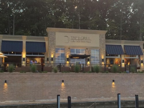 Exterior view of Tap & Grill Lakeside Brew Haus, featuring a stone facade and outdoor seating by the water.