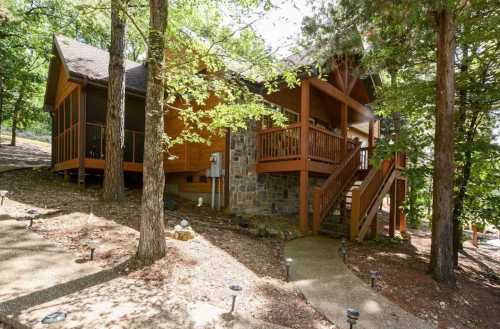 A charming wooden cabin with stone accents, surrounded by trees and a winding pathway.