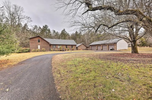 A rustic wooden house with a gravel driveway, surrounded by trees and a garage in a serene, rural setting.