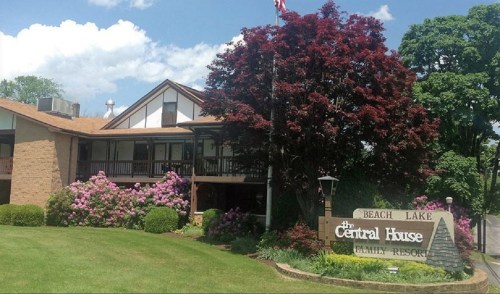 A charming resort building surrounded by vibrant flowers and trees, with a sign reading "The Central House Family Resort."