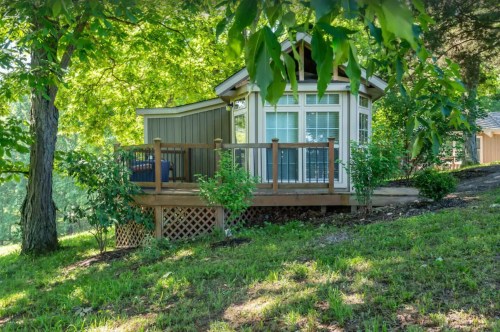 A cozy cabin with a deck surrounded by lush greenery and trees on a sunny day.