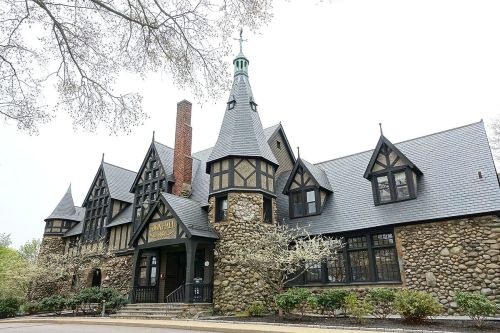 A large, ornate stone and wood building with a steep roof and decorative spires, surrounded by trees and greenery.