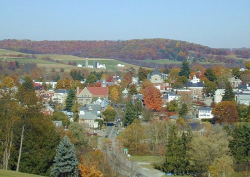 A scenic view of a small town surrounded by colorful autumn foliage and rolling hills in the background.