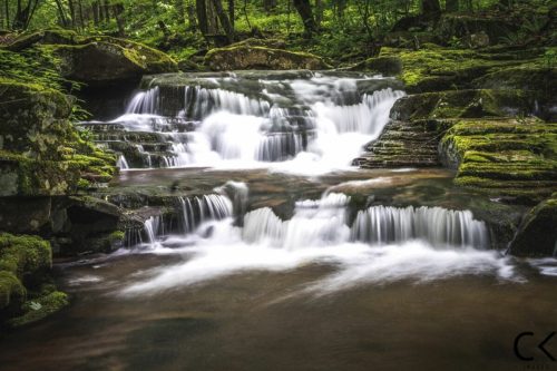 A serene waterfall cascades over moss-covered rocks in a lush green forest.