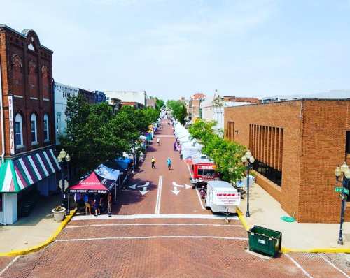 A view of a bustling street lined with tents and vendors, showcasing a vibrant market atmosphere on a sunny day.