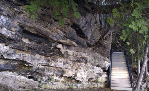 A stone staircase leads up from a rocky area, surrounded by greenery and natural rock formations.