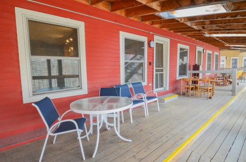 A porch with a round table and chairs, featuring a red wall and wooden flooring, under a covered area.