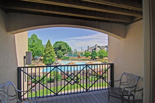 View from a balcony overlooking a pool area surrounded by greenery and landscaped gardens.