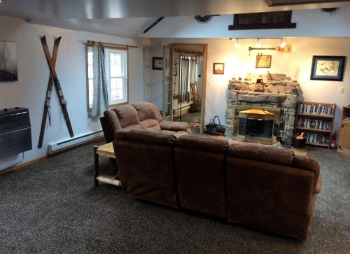 Cozy living room with a stone fireplace, brown couch, wooden coffee table, and vintage skis on the wall.