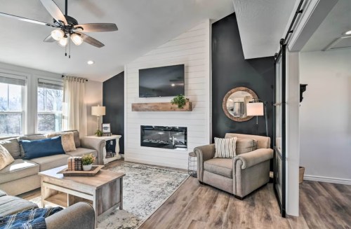 Cozy living room with a modern fireplace, comfortable seating, and large windows, featuring neutral tones and stylish decor.