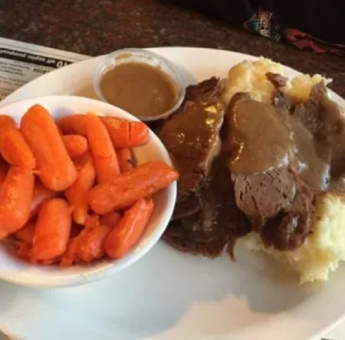 A plate of mashed potatoes topped with gravy, sliced roast beef, and a side of glazed carrots.