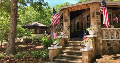 A charming lodge entrance with stone steps, surrounded by greenery and decorated with American flags.