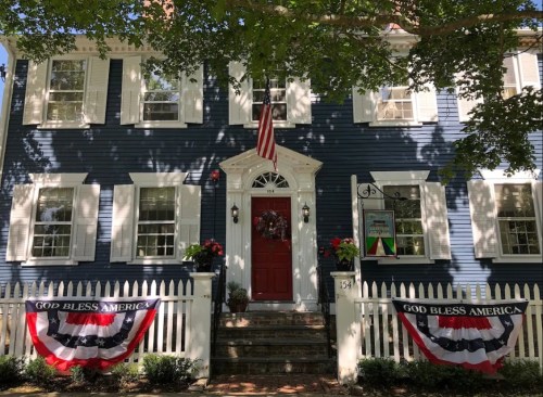 A blue house with white shutters, a red door, and patriotic decorations, including banners and an American flag.