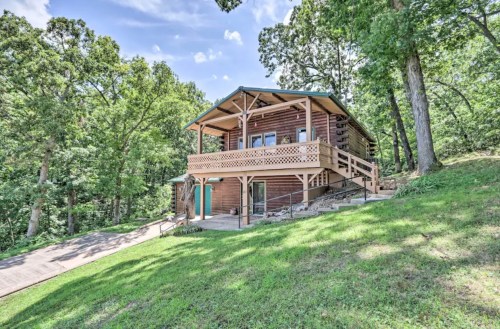 A wooden cabin surrounded by trees, featuring a porch and steps leading up to the entrance.