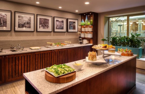 A modern buffet setup featuring fresh vegetables, appetizers, and framed photos on the wall in a well-lit space.