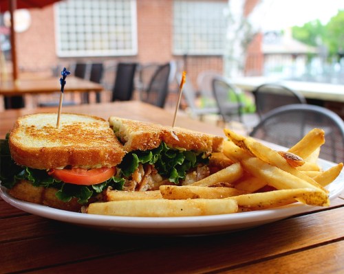 A close-up of a sandwich with lettuce and tomato, served with a side of golden fries on a wooden table.