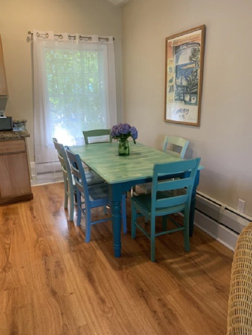 A light green table surrounded by blue chairs, with a vase of flowers, in a bright, airy dining area.