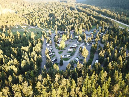 Aerial view of a campground surrounded by dense forest, with RVs and tents arranged in a circular layout.