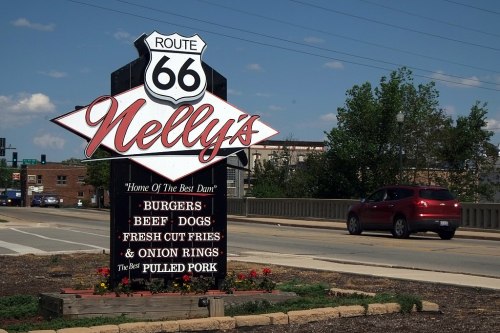 Sign for Nelly's on Route 66, featuring menu items like burgers, beef dogs, fries, and pulled pork.